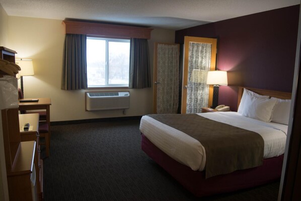 A hotel room with a bed, bedside table, lamp, air conditioning unit, window with curtains, and a telephone.