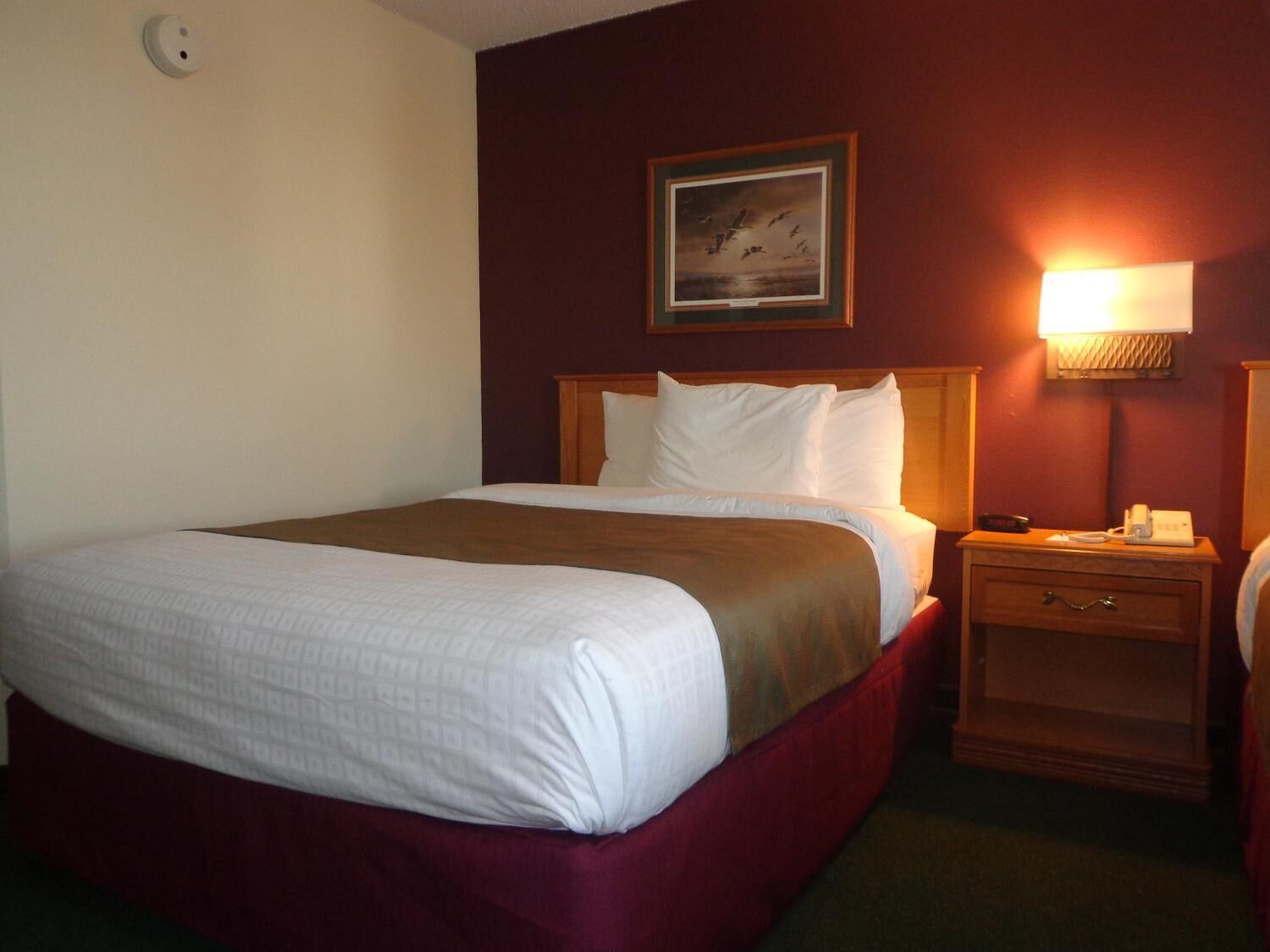 A hotel room with a large bed, a bedside table with a lamp, and a painting on the wall.