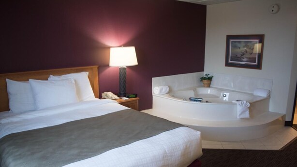 A hotel room with a large bed, a bedside table with a lamp, a telephone, and a round bathtub. - AmericInn by Wyndham Madison SD (Madison)