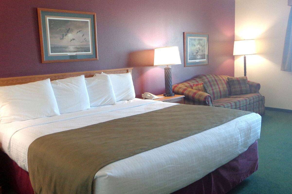 A hotel room with a large bed, a chair, two lamps, and two framed pictures on the wall.