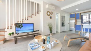 Ein modernes Wohnzimmer mit Fernseher, rundem Tisch mit Zeitschrift, Couchtisch und Sofa.