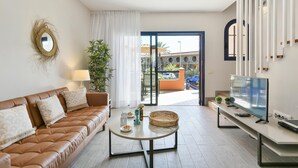 Ein modernes Wohnzimmer mit einer Ledersofa, einem runden Couchtisch, einem Flachbildfernseher und einem Balkon mit Blick auf ein Gebäude.
