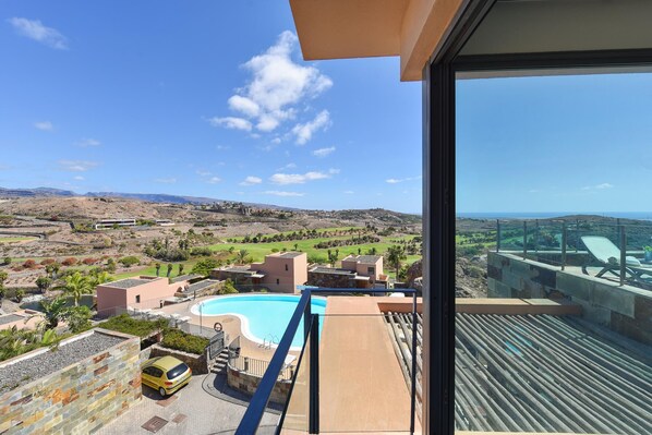 A balcony with a pool, a view of a hilly landscape, and a clear sky.
