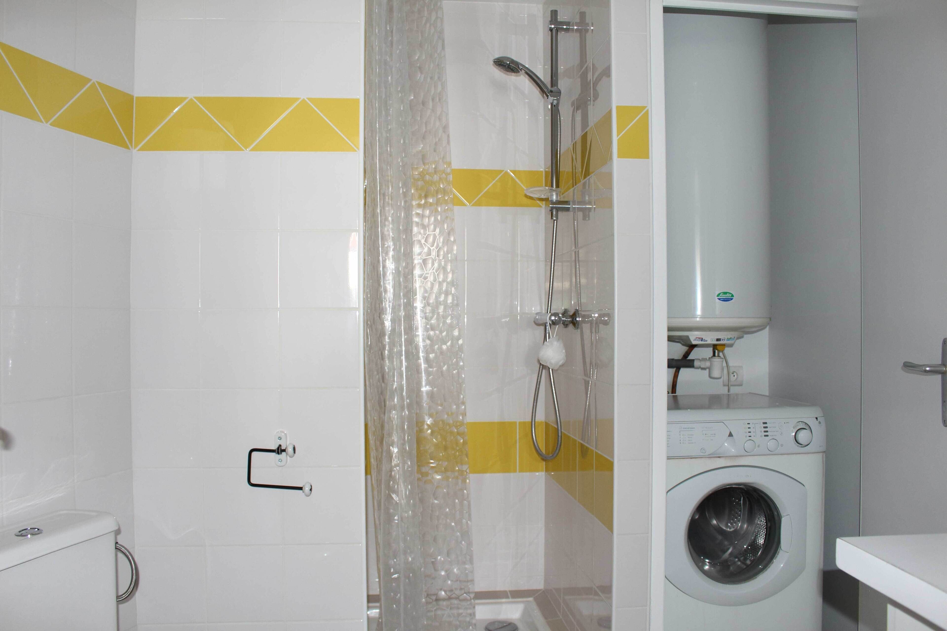 Een badkamer met een douche, toilet en een wasmachine.
