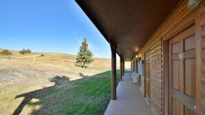A covered wooden building with a porch, a grassy area, and a tree.