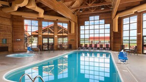 An indoor swimming pool with clear views of the outside, wooden architecture, and lounge chairs.