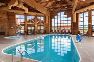 An indoor swimming pool with clear views of the outside, wooden architecture, and lounge chairs.