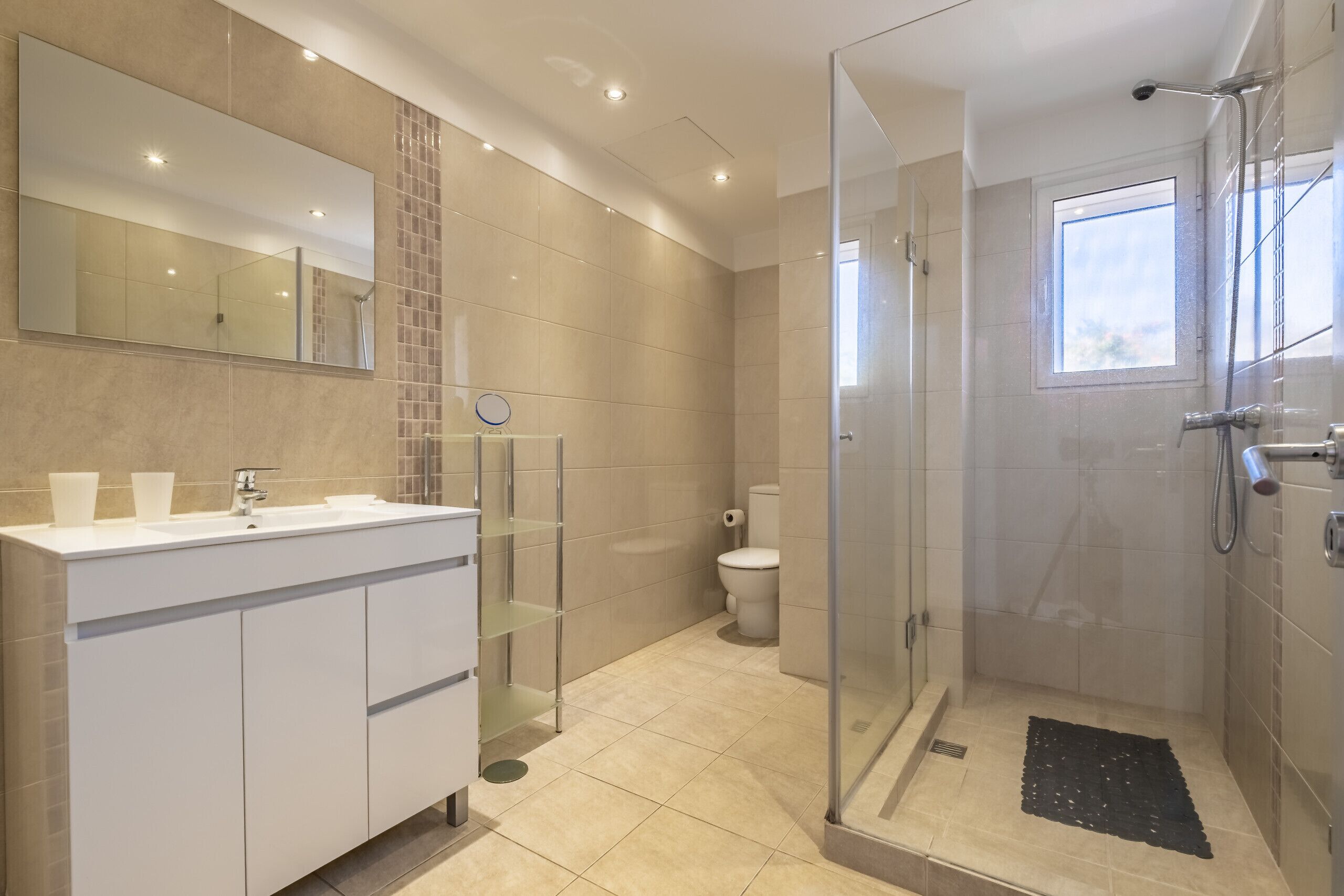 Un baño moderno con ducha envuelta en vidrio, un espejo grande y un tocador blanco.