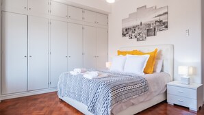 Une chambre à coucher avec un lit, une armoire blanche et une œuvre d’art représentant un paysage urbain accrochée au mur.