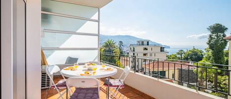 A balcony with a table set for breakfast, overlooking a scenic view of buildings and mountains.