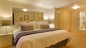 A bedroom with a large bed, a nightstand, a mirror, and a wardrobe. - Angel Cottage (Cape Town)