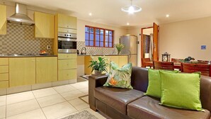 A modern kitchen with yellow cabinets, stainless steel appliances, and a window with red frames. - Angel Cottage (Cape Town)