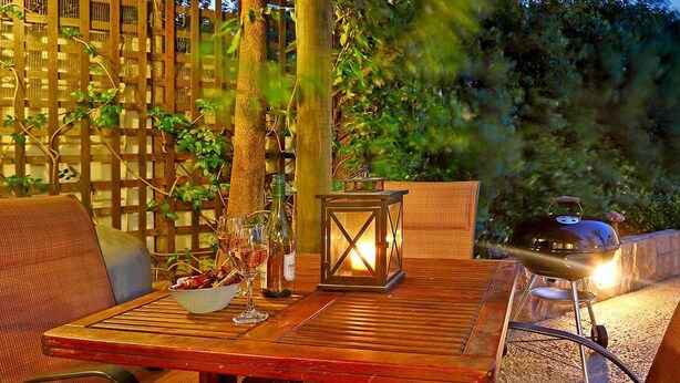 An outdoor wooden deck with a table set for dining, surrounded by wicker chairs. - Angel Cottage (Cape Town)