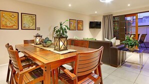 A dining area with a wooden table and chairs, a sofa, and a TV mounted on the wall. - Angel Cottage (Cape Town)