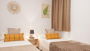 A hotel room with two beds, a nightstand with a lamp, a wall-mounted mirror, and a framed botanical print.