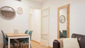 A room with a dining table, chairs, a sofa, a mirror, and a clock on the wall.