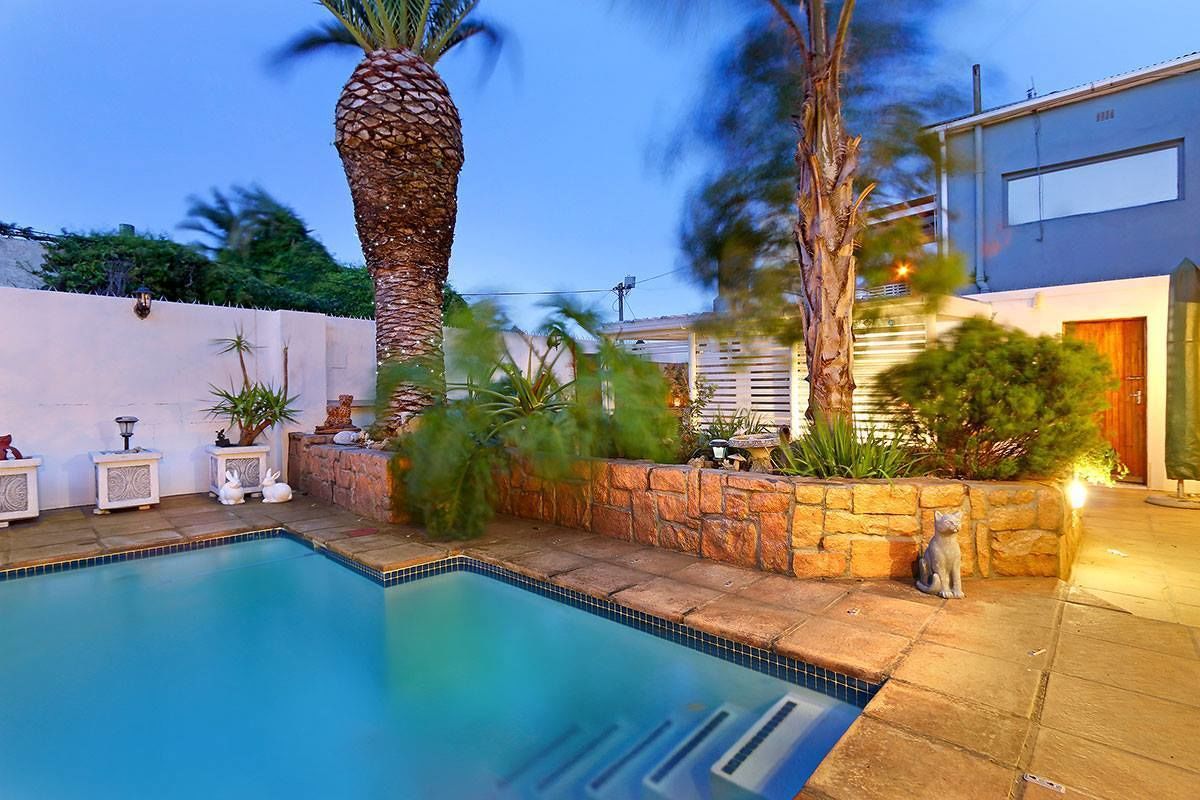 Una piscina con borde de piedra, palmeras y una estatua de gato.