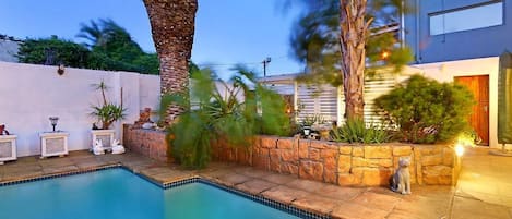 Una piscina con borde de piedra, palmeras y una estatua de gato.