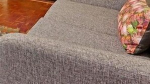 Una sala de estar moderna con un sofá gris, una mesita con un jarrón de girasoles y vistas a un paisaje urbano nocturno a través de amplios ventanales.