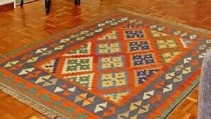 Una cocina compacta con armarios blancos, un microondas y un frutero en la encimera. Hay dos taburetes negros y una alfombra estampada sobre el suelo de madera.