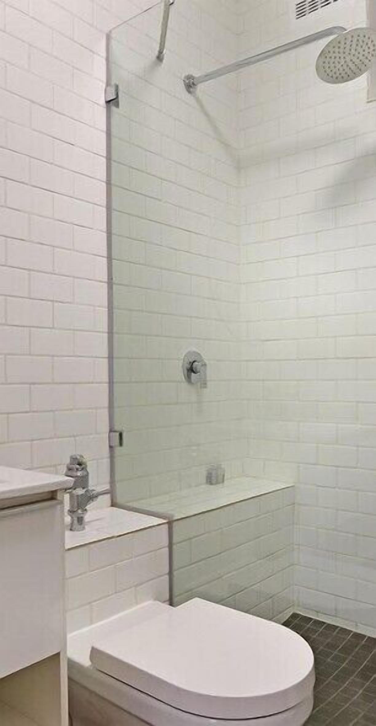 A modern bathroom with white subway tiles, a glass shower enclosure, a toilet, and a sink.