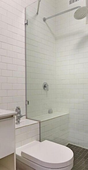 Un baño moderno con azulejos blancos tipo metro, cabina de ducha de vidrio, inodoro y lavamanos.