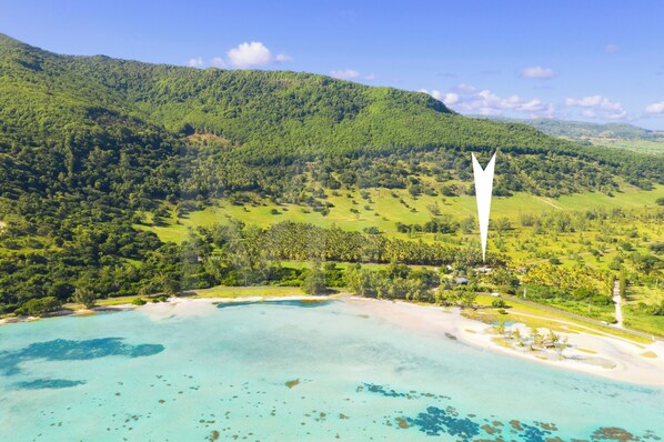 A coastal landscape with a prominent white tower, lush green hills, and clear turquoise waters.