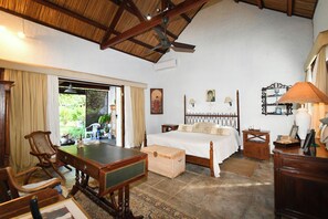 A bedroom with a bed, a wooden table, a chair, a desk, and a ceiling fan.