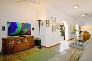 A living room with a flat-screen TV, wooden cabinet, floor lamp, and a sofa. - Villa La Cocoteraie, 400 sqm, close to the beach, in a beautiful garden (Baie du Cap)