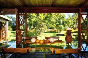 Ein Essbereich im Freien mit einem Glastisch, Holzstühlen und einer Holzbank. Auf dem Tisch liegen Ananas und Orangen.