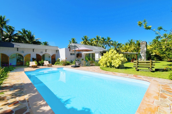 A swimming pool with lounge chairs, a stone pathway, and a building with arched windows.