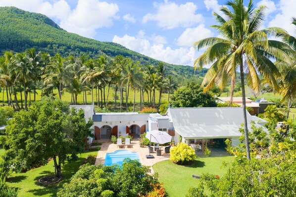 A resort with a swimming pool, outdoor seating, and a view of lush greenery and hills. - Villa La Cocoteraie, 400 sqm, close to the beach, in a beautiful garden (Baie du Cap)