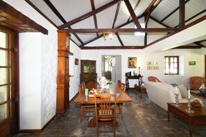 A dining area with a long wooden table, chairs, and a chandelier. There is a sofa and a side table with a lamp in the background. - Villa La Cocoteraie, 400 sqm, close to the beach, in a beautiful garden (Baie du Cap)