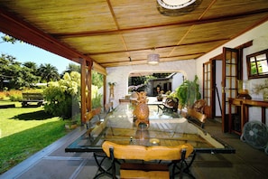 A covered outdoor dining area with a glass table, wooden chairs, and a fan.