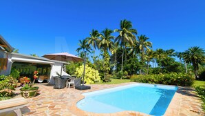 Piscina con baldosas de piedra, rodeada de palmeras y un patio con mobiliario exterior.
