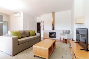 A modern living room with a sofa, a wooden coffee table, a fireplace, and a television.