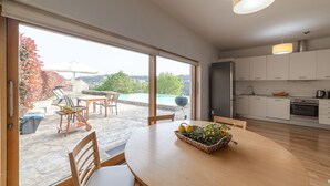 A modern kitchen with white cabinets, a dining area with a round table, and a view of a swimming pool and garden through large windows.