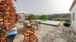 A stone patio with a pool, outdoor furniture, and a barbecue grill.