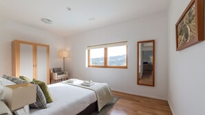 A modern hotel room with a large bed, a desk, a chair, a lamp, and a window with a view.