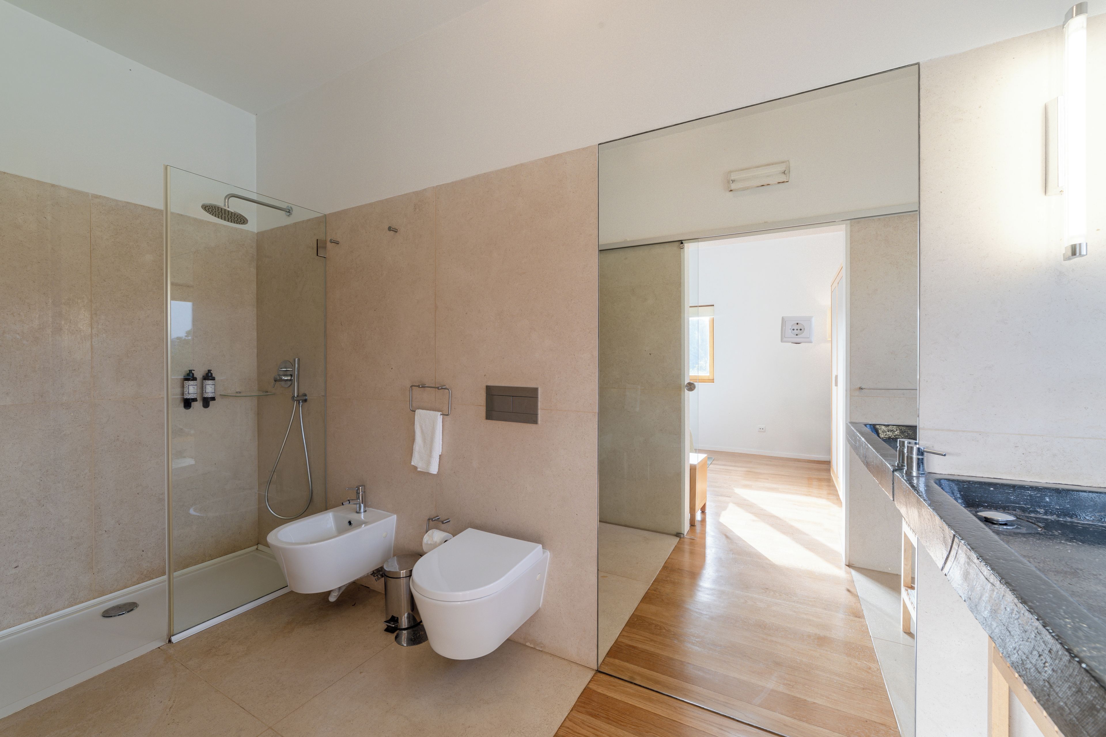 Een moderne badkamer met een glazen douchecabine, een bidet en een toilet.