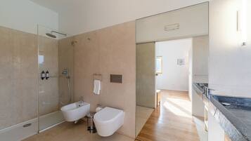 Een moderne badkamer met een glazen douchecabine, een bidet en een toilet.