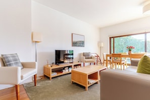 A modern living room with a flat-screen TV, a sofa, a coffee table, and a dining area with a table and chairs. - A Retreat with a Natural Pool Bathed by the Douro River (Gondomar)