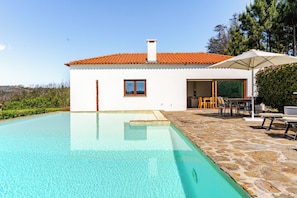 A house with a swimming pool, a covered patio, and a view of the surrounding landscape.