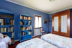 Un dormitorio con dos camas, una estantería, una silla y un armario.