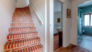 Una escalera de ladrillo rojo y barandas blancas que conduce a una habitación con una cama y un ventanal.