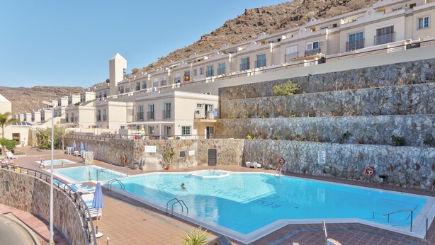 A swimming pool with a stone wall and a view of hotel buildings. - Luxury apartment in Puerto Rico (Mogán) (Mogán)