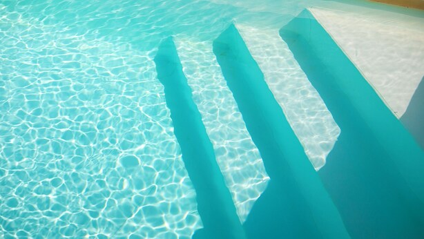 A clear pool with visible ripples and shadows of poolside structures.