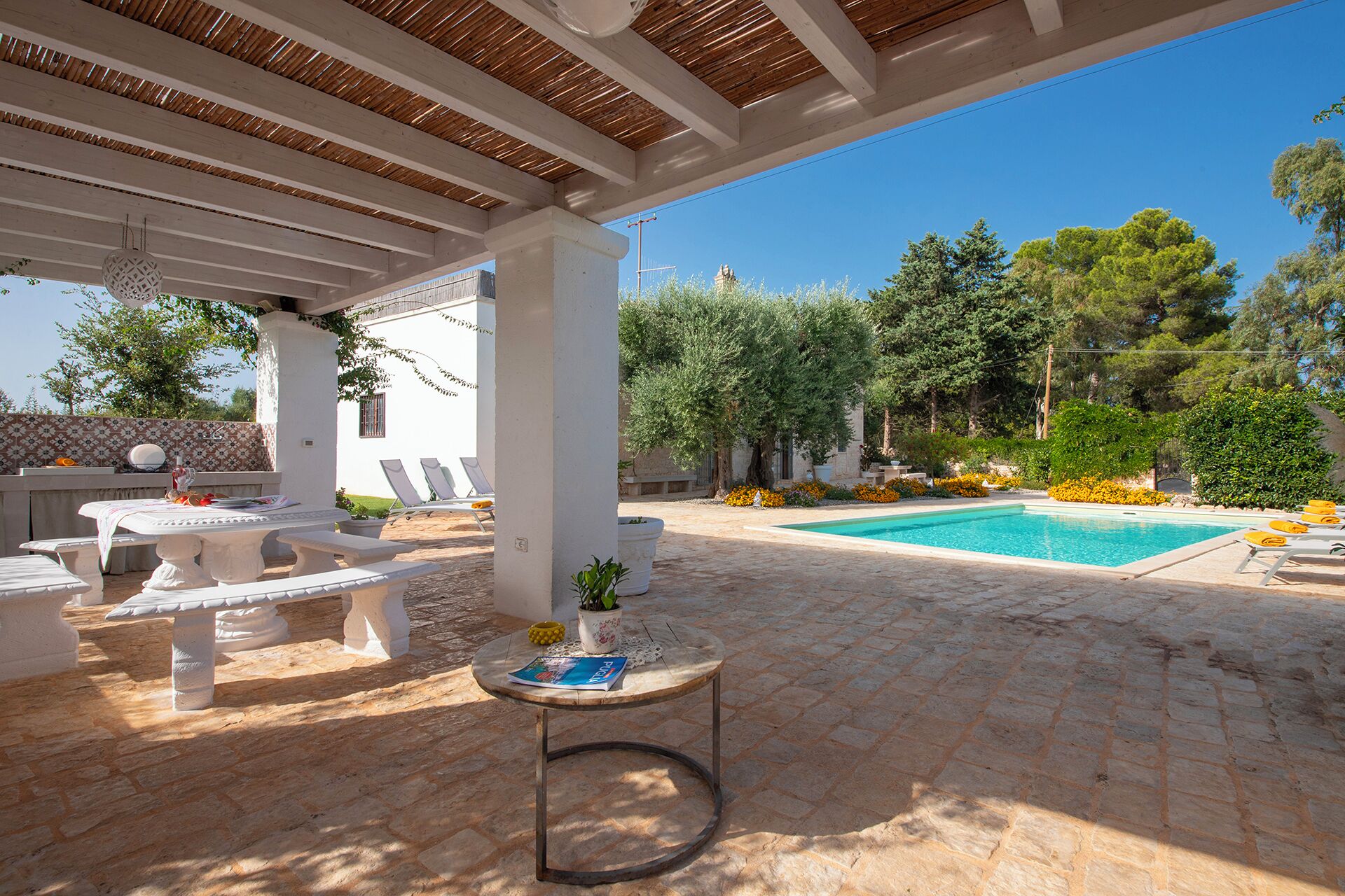 A covered outdoor area with a pool, lounge chairs, and a table with a book.