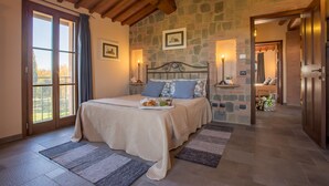 A bedroom with a stone wall, a large bed with a tray of pastries, and a view through a glass door. - Special Offer! Holidays, (Villa Lestra 8 + 3) Area Volterra, San Gimignano, Pisa (Pisa)