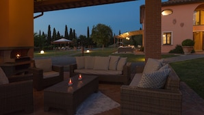An outdoor patio with wicker furniture, a fire pit, and a view of a residential area at dusk. - Special Offer! Holidays, (Villa Lestra 8 + 3) Area Volterra, San Gimignano, Pisa (Pisa)